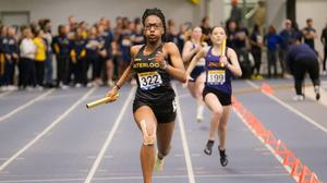 Female athlete running with baton on indoor track 
